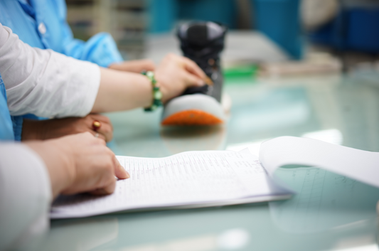 Two people's hands touching a sneaker boot shoe and reviewing a check list on a pad of paper ensuring the highest attention to detail and quality in Deckers Lab footwear
